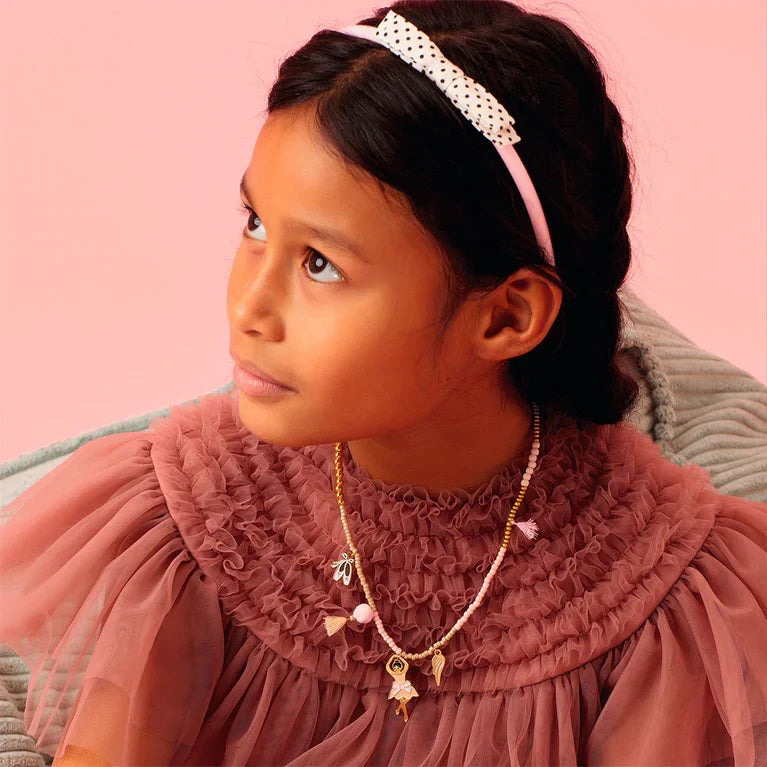 Young girl wearing a pink dress with ruffled collar and headband against a pink background