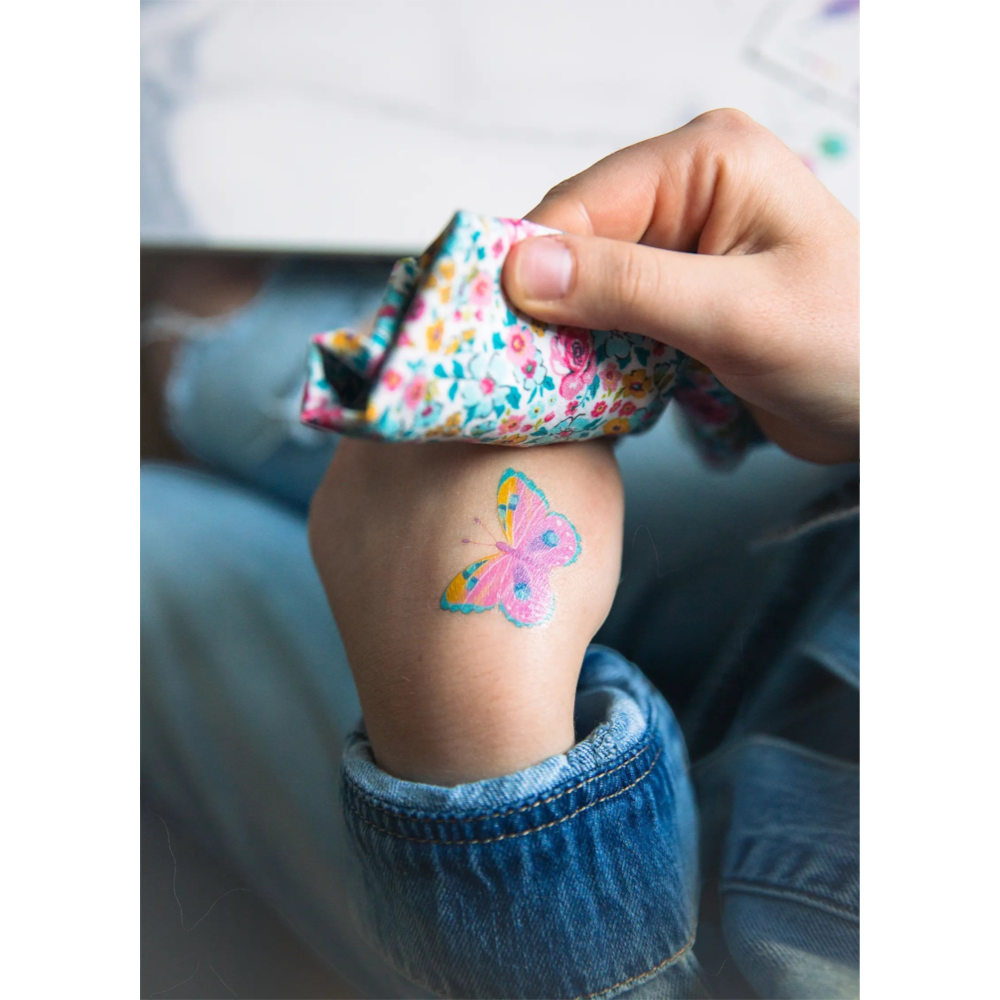 One Two Play butterfly temporary tattoo on a child's arm with a floral patterned cloth held nearby.